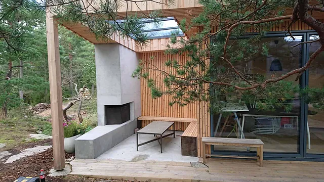 Overbygd uteplass med peis, sittebenker og trekledning integrert i moderne hytte.